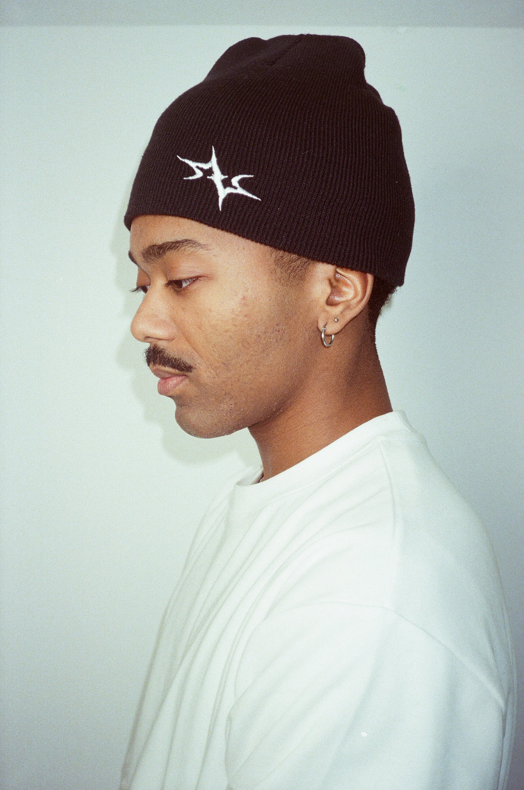 Person wearing a black beanie with a white logo on a light gray background